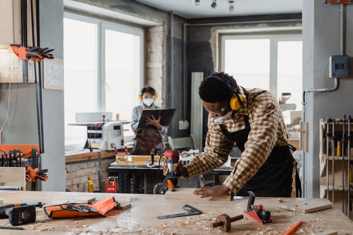 A craftsman routing wood at a workbench in a workshop